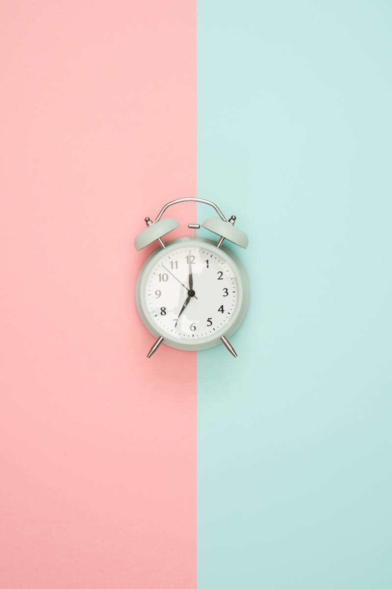 A vintage round clock on a split pastel pink and blue background.